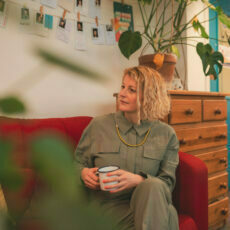 Jen McCanna sitting down on red sofa with coffee