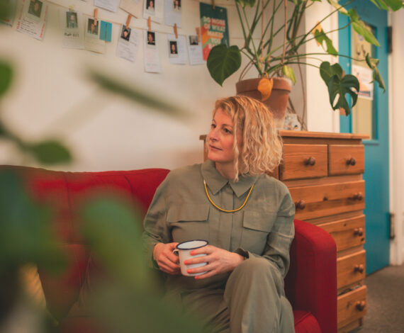 Jen McCanna sitting down on red sofa with coffee